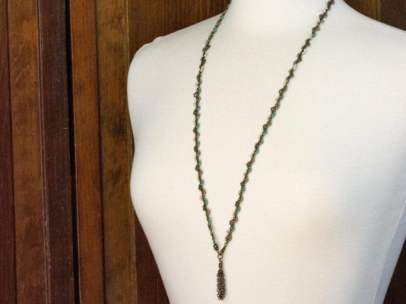 May include: A long, delicate necklace with a bronze chain and turquoise beads. The necklace has a tassel pendant at the bottom.