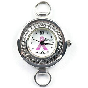 May include: A silver tone watch with a white face and a pink ribbon design. The watch has a round face with a rope-like border. The watch is attached to a silver tone chain with two loops.