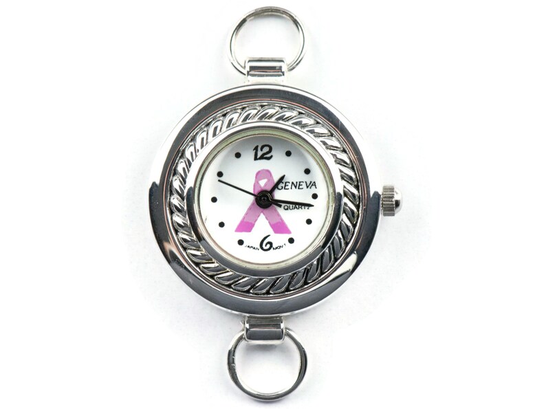 May include: A silver tone watch with a white face and a pink ribbon design. The watch has a round face with a rope-like border. The watch is attached to a silver tone chain with two loops.