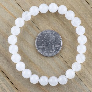 May include: White beaded bracelet made of round, opaque white beads. The bracelet is approximately the size of a US quarter.