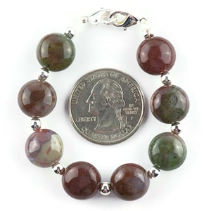 May include: A bracelet made with round, brown, green, and white agate beads with silver spacers and a silver clasp. The bracelet is shown next to a US quarter for size reference.