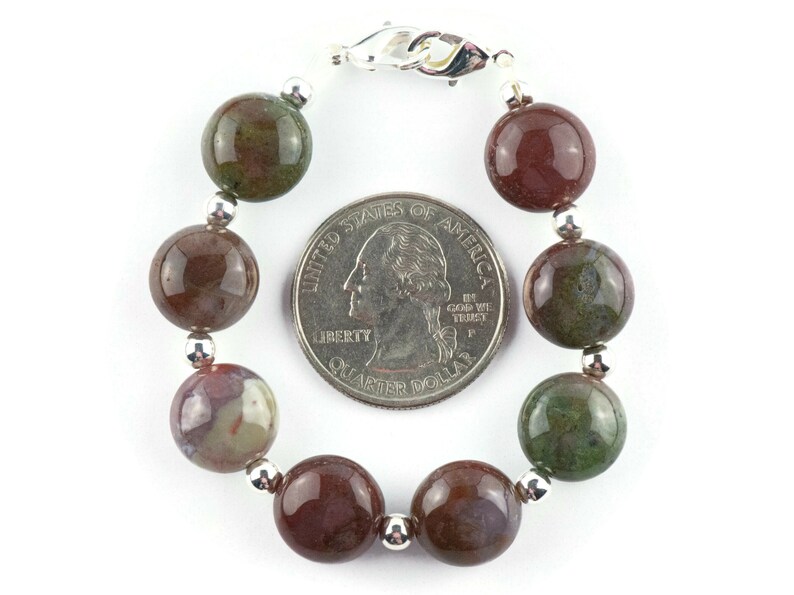 May include: A bracelet made with round, brown, green, and white agate beads with silver spacers and a silver clasp. The bracelet is shown next to a US quarter for size reference.