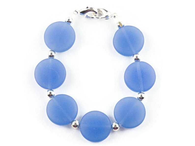 Peut inclure: Un bracelet bleu clair avec des perles rondes et un fermoir argent&eacute;.