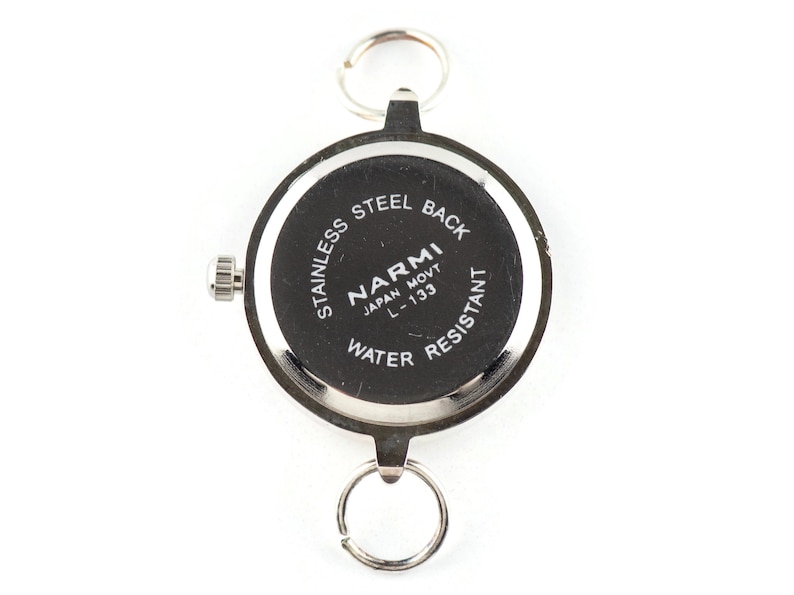 May include: A round silver-tone watch case with a black back featuring the text STAINLESS STEEL BACK, NARMI, JAPAN MOVT, L-133, and WATER RESISTANT. The watch includes a side crown and two silver metal rings attached to the top and bottom lugs.