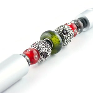 May include: A silver pen with a series of colourful beads, including red, green, and black. The beads are made of glass and metal.