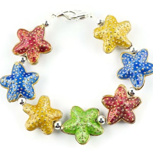 Puede incluir: Un brazalete de plata con seis abalorios de estrella de mar de esmalte de colores. Los abalorios son rojos, azules, amarillos y verdes.