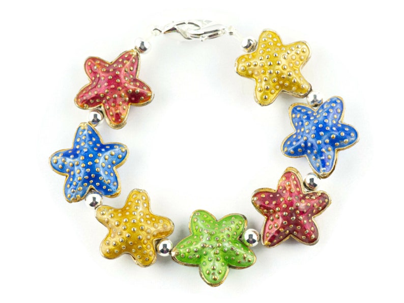 Puede incluir: Un brazalete de plata con seis abalorios de estrella de mar de esmalte de colores. Los abalorios son rojos, azules, amarillos y verdes.