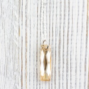 May include: A silver chain necklace with a faceted, rectangular, light amber crystal pendant.