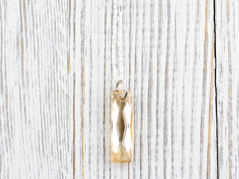 May include: A silver chain necklace with a faceted, rectangular, light amber crystal pendant.
