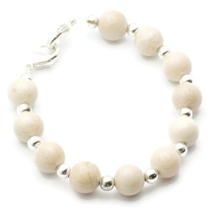 Op de afbeelding: Een witte kralen armband met zilveren accenten. De armband is gemaakt van ronde, gladde kralen en heeft een zilveren sluiting.