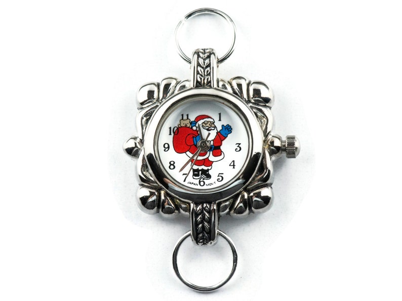 May include: A silver pocket watch with a white face and a Santa Claus design. The watch has a silver chain and a silver clasp.