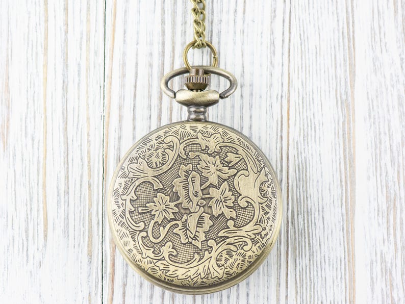 May include: A gold pocket watch with a floral design on the front. The watch is hanging from a chain.
