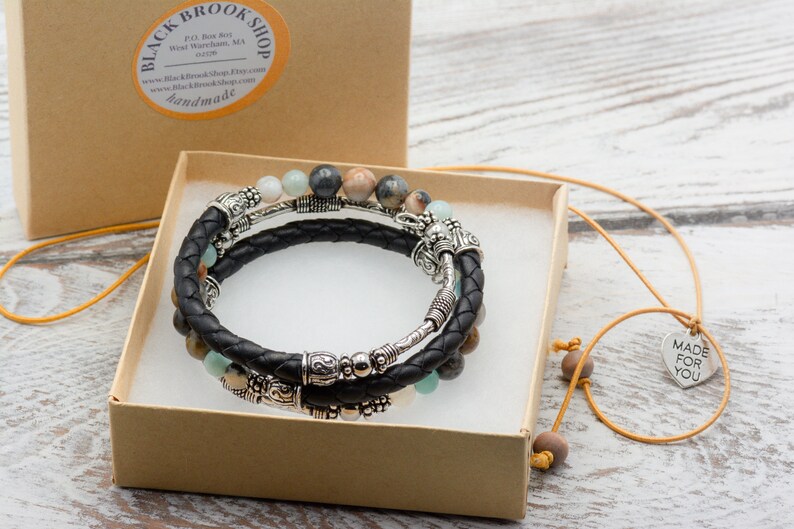 May include: A set of three bracelets with black leather cord, silver beads, and gemstone beads. The bracelets are in a brown box with a yellow ribbon. A necklace with a silver heart pendant that says "Made for You" is also included.