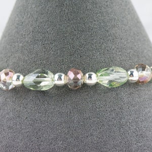 May include: A delicate bracelet featuring alternating clear, green, and iridescent pink glass beads with silver spacers.