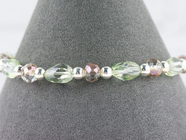 May include: A delicate bracelet featuring alternating clear, green, and iridescent pink glass beads with silver spacers.