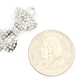 Puede incluir: Encanto de lazo plateado con diamantes de imitaci&oacute;n transparentes. El encanto es aproximadamente del tama&ntilde;o de una moneda de 25 centavos de d&oacute;lar estadounidense.