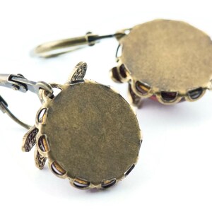 Pode incluir: Um par de brincos de bronze com um design floral e uma pedra vermelha no centro. Os brincos s&atilde;o mostrados por tr&aacute;s, revelando o suporte de metal.