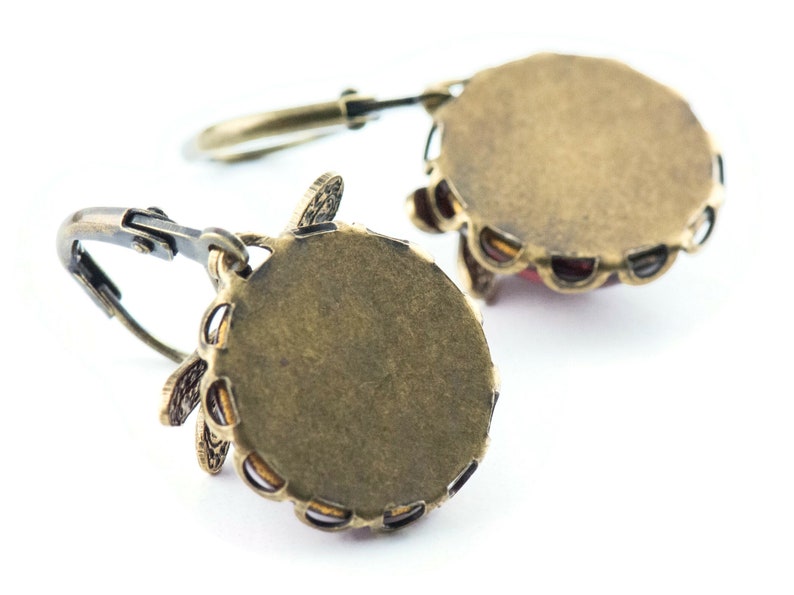 Pode incluir: Um par de brincos de bronze com um design floral e uma pedra vermelha no centro. Os brincos s&atilde;o mostrados por tr&aacute;s, revelando o suporte de metal.