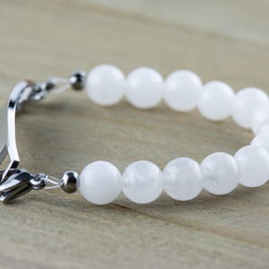 May include: A white gemstone bracelet with a silver clasp and a silver tag engraved with the word "Mama".