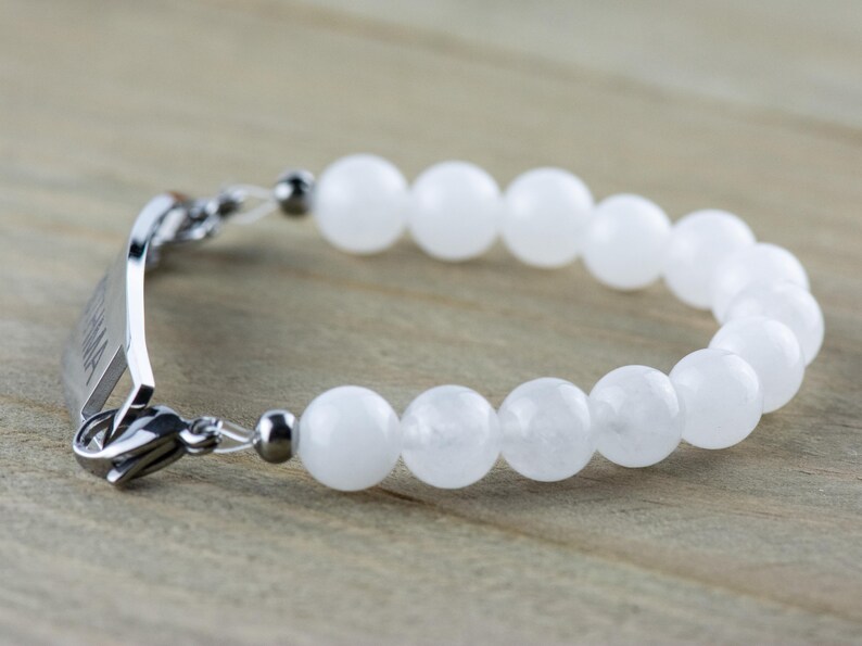 May include: A white gemstone bracelet with a silver clasp and a silver tag engraved with the word "Mama".
