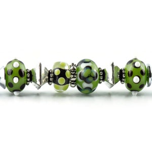 May include: A silver pen with green and white polka dot beads and a green and white patterned bead.