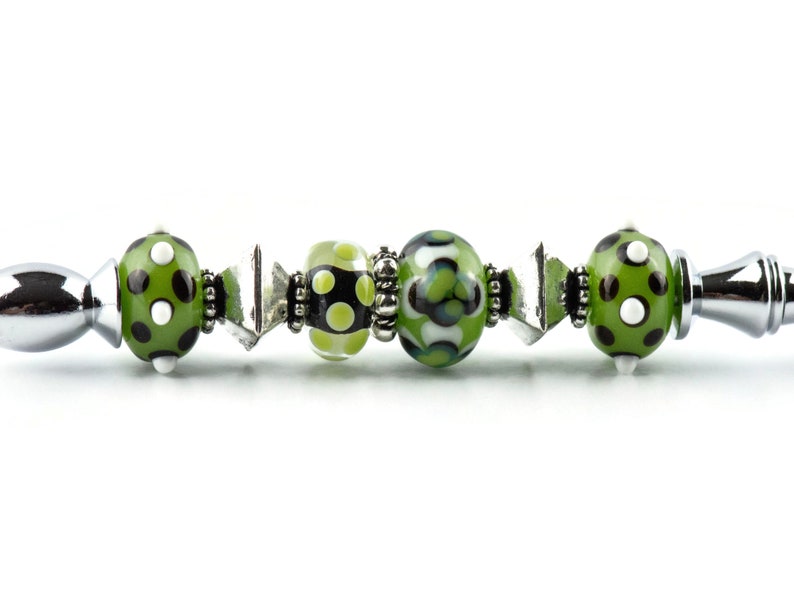 May include: A silver pen with green and white polka dot beads and a green and white patterned bead.