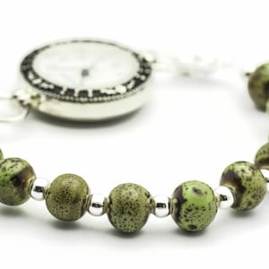 May include: A silver pocket watch with a white face and black markings is attached to a bracelet with green and brown beads.