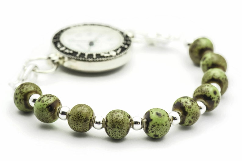May include: A silver pocket watch with a white face and black markings is attached to a bracelet with green and brown beads.
