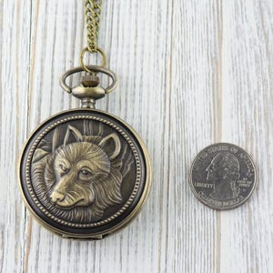 May include: A bronze pocket watch with a wolf design on the face. The watch is about the size of a quarter.