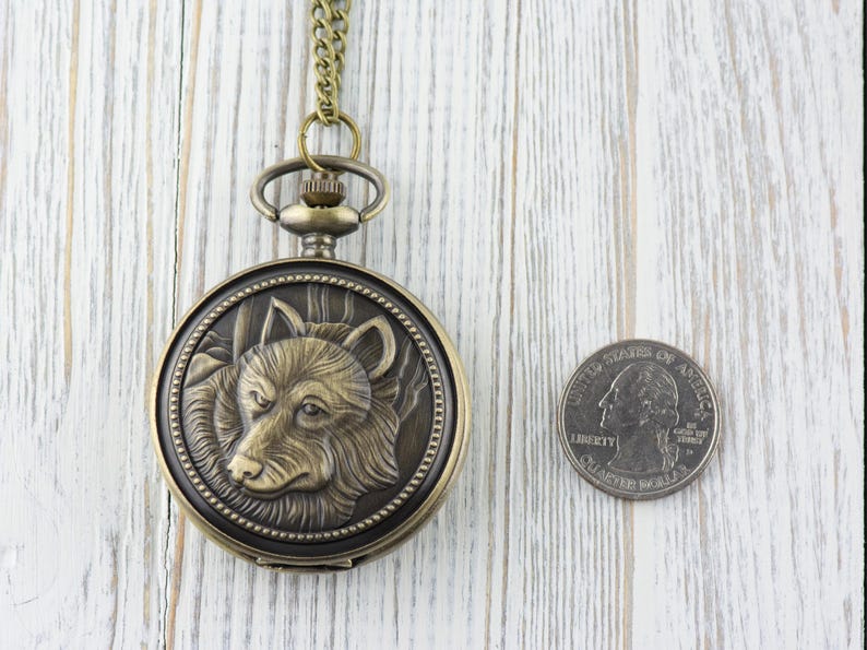 May include: A bronze pocket watch with a wolf design on the face. The watch is about the size of a quarter.