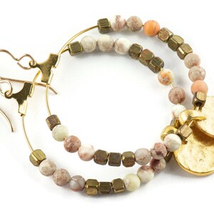 May include: Gold hoop earrings with brown, white, and peach colored beads and two gold charms.