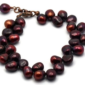 May include: A bracelet made of dark red freshwater pearls. The pearls are irregularly shaped and have a high luster. The bracelet has a copper clasp.