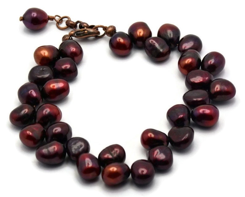 May include: A bracelet made of dark red freshwater pearls. The pearls are irregularly shaped and have a high luster. The bracelet has a copper clasp.