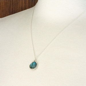 Pu&ograve; includere: Una collana d'argento con un ciondolo a forma di goccia con una pietra color turchese. Il ciondolo &egrave; incastonato in una lunetta d'argento e pende da una sottile catena d'argento. La collana &egrave; mostrata su uno sfondo bianco.