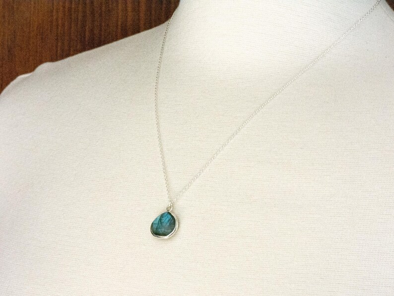 Pu&ograve; includere: Una collana d'argento con un ciondolo a forma di goccia con una pietra color turchese. Il ciondolo &egrave; incastonato in una lunetta d'argento e pende da una sottile catena d'argento. La collana &egrave; mostrata su uno sfondo bianco.