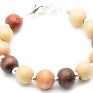Puede incluir: Un brazalete de cuentas de madera con un cierre plateado. Las cuentas son en tonos de marr&oacute;n, beige y rosa.