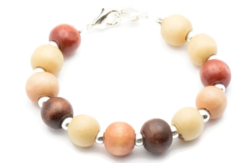 Puede incluir: Un brazalete de cuentas de madera con un cierre plateado. Las cuentas son en tonos de marr&oacute;n, beige y rosa.
