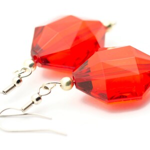 May include: A pair of red crystal earrings with silver hooks. The crystals are faceted and have a geometric shape.