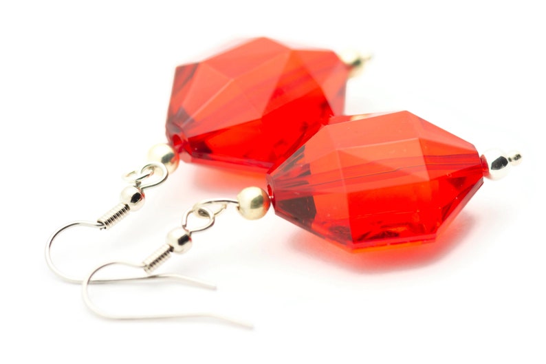 May include: A pair of red crystal earrings with silver hooks. The crystals are faceted and have a geometric shape.