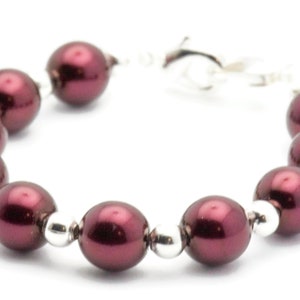 May include: A burgundy pearl bracelet with silver accents. The bracelet is made of round pearls and silver beads.