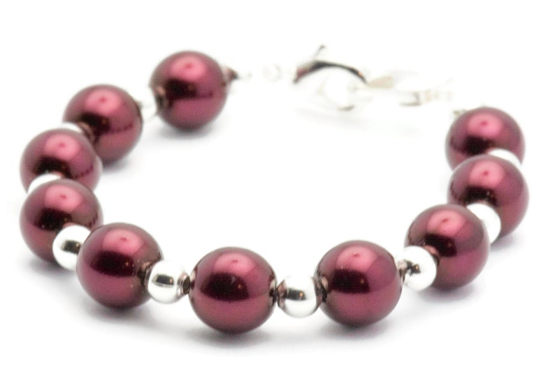 May include: A burgundy pearl bracelet with silver accents. The bracelet is made of round pearls and silver beads.