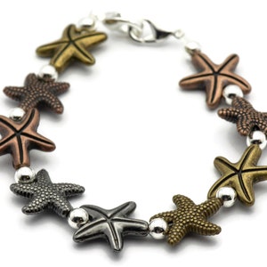 May include: A silver chain bracelet with a lobster clasp features a series of star-shaped charms in various metallic finishes, including gold, copper, and gunmetal.