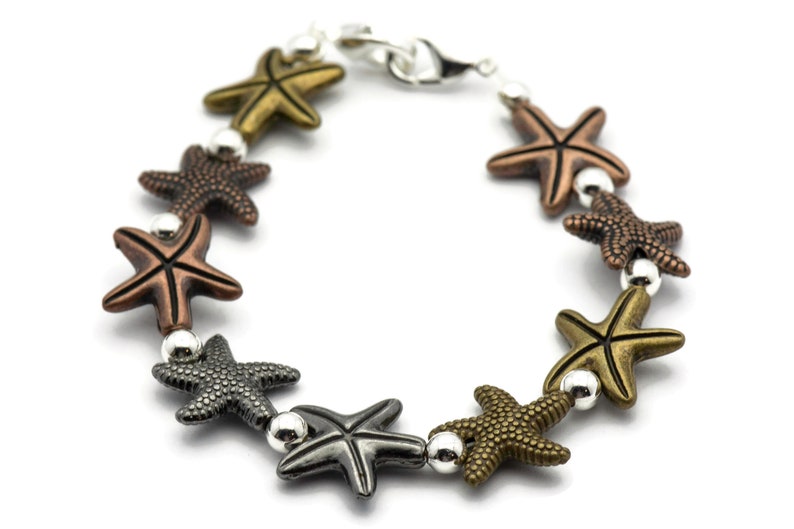 May include: A silver chain bracelet with a lobster clasp features a series of star-shaped charms in various metallic finishes, including gold, copper, and gunmetal.