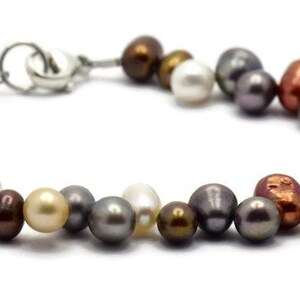 May include: A multi-colored pearl bracelet with a silver clasp. The pearls are in shades of white, cream, gray, brown, copper, and blue.
