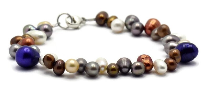 May include: A multi-colored pearl bracelet with a silver clasp. The pearls are in shades of white, cream, gray, brown, copper, and blue.