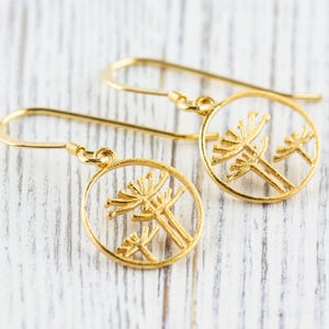 May include: A pair of gold dangle earrings with a circular design featuring a delicate cutout of two stylized flowers.