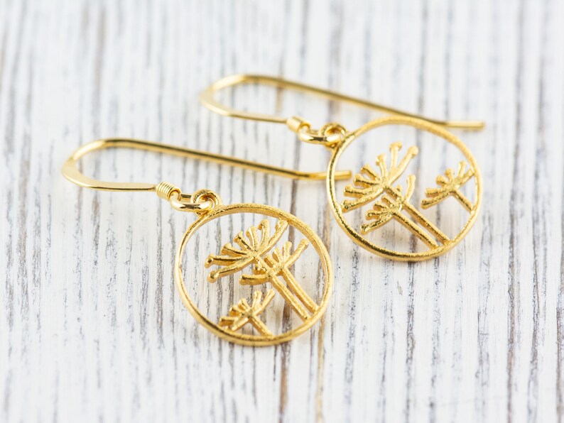 May include: A pair of gold dangle earrings with a circular design featuring a delicate cutout of two stylized flowers.