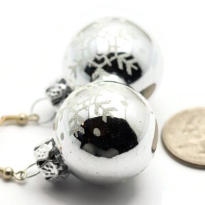 May include: Silver snowflake ornament earrings with a silver hook. The earrings are about the size of a quarter.