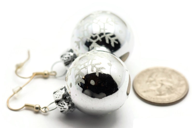 May include: Silver snowflake ornament earrings with a silver hook. The earrings are about the size of a quarter.