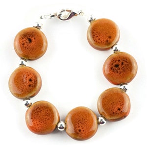 May include: A bracelet made with round, orange ceramic beads and silver spacers. The bracelet has a silver clasp.